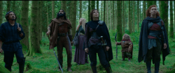 Several people in fantasy medieval garb in a dark forest.