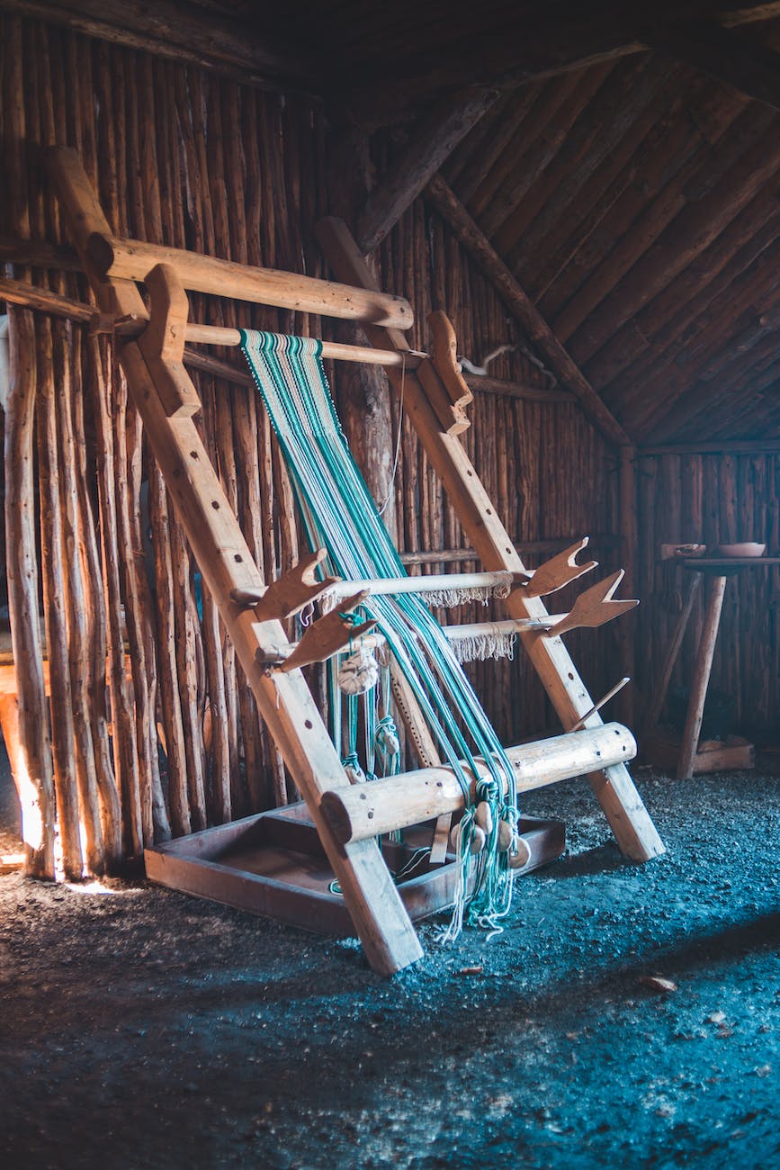 A vertical loom in a wooden branch shack. The threads on the loom are blue