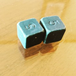 Two old d6 showing the number 5. They are a green like the color of exposed old copper.